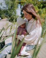 Maman tenant bébé dans ses bras dehors avec doudou rose antique.
